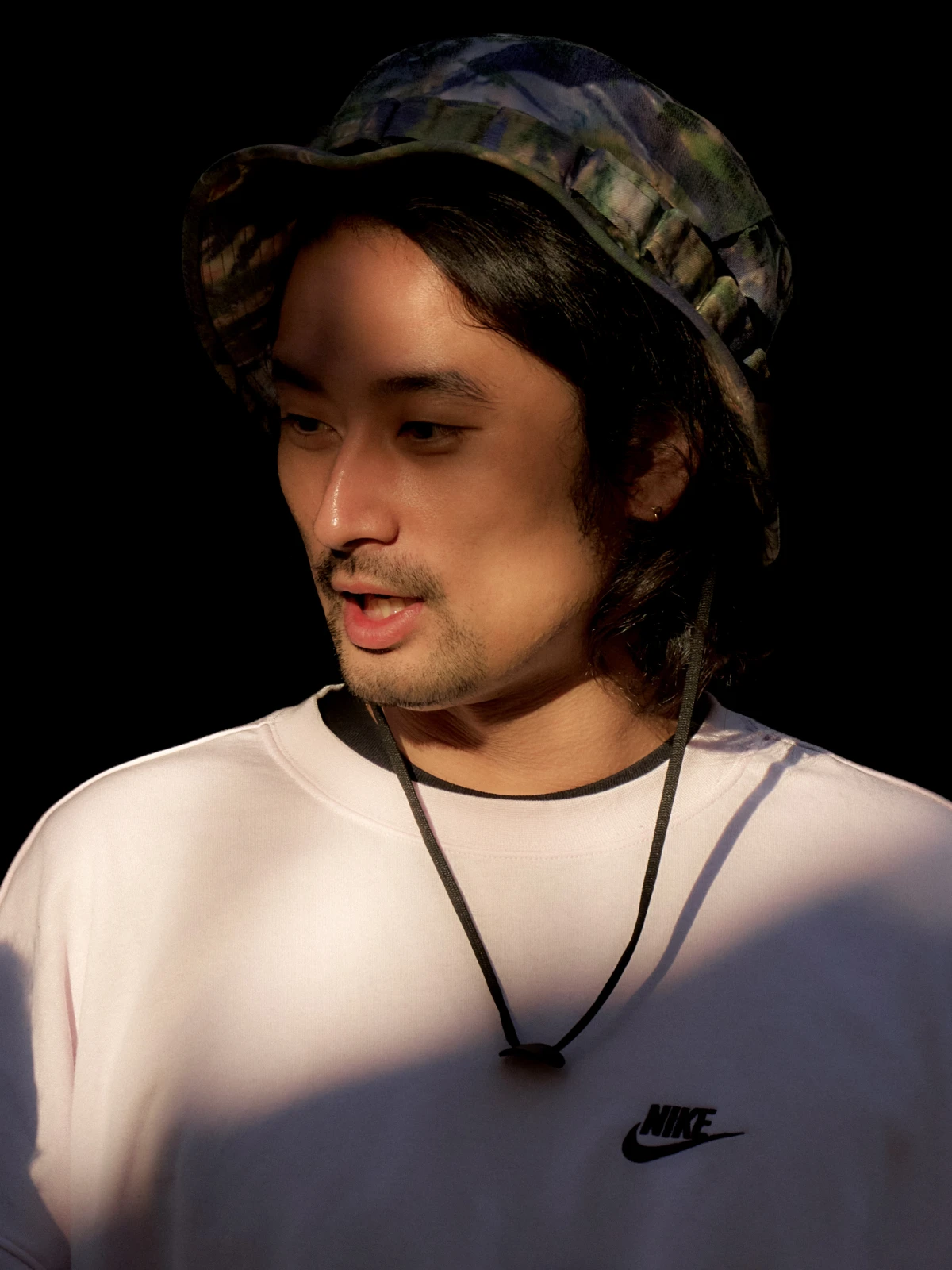 Young man in Nike sweatshirt and cap in dramatic studio light for sportswear portrait campaign