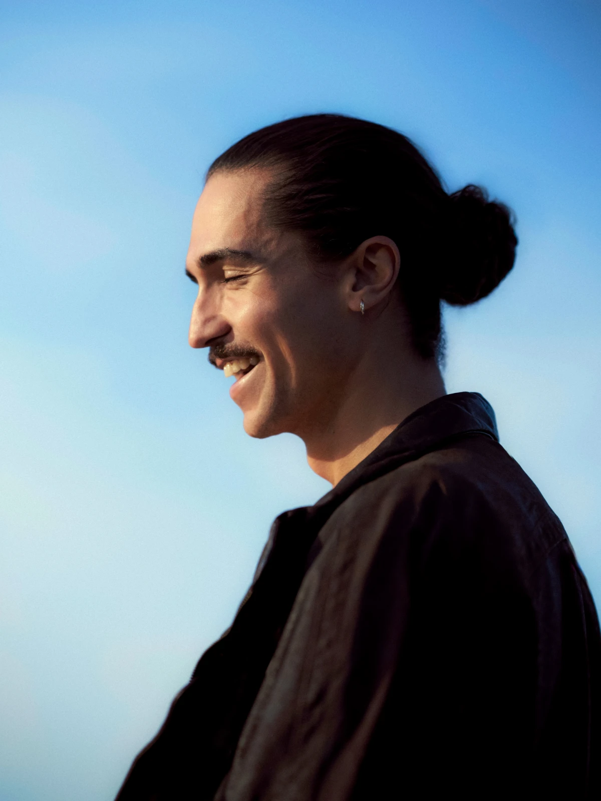 Profile portrait of smiling man with tied hair against blue sky for ZEIT Wissen editorial portrait