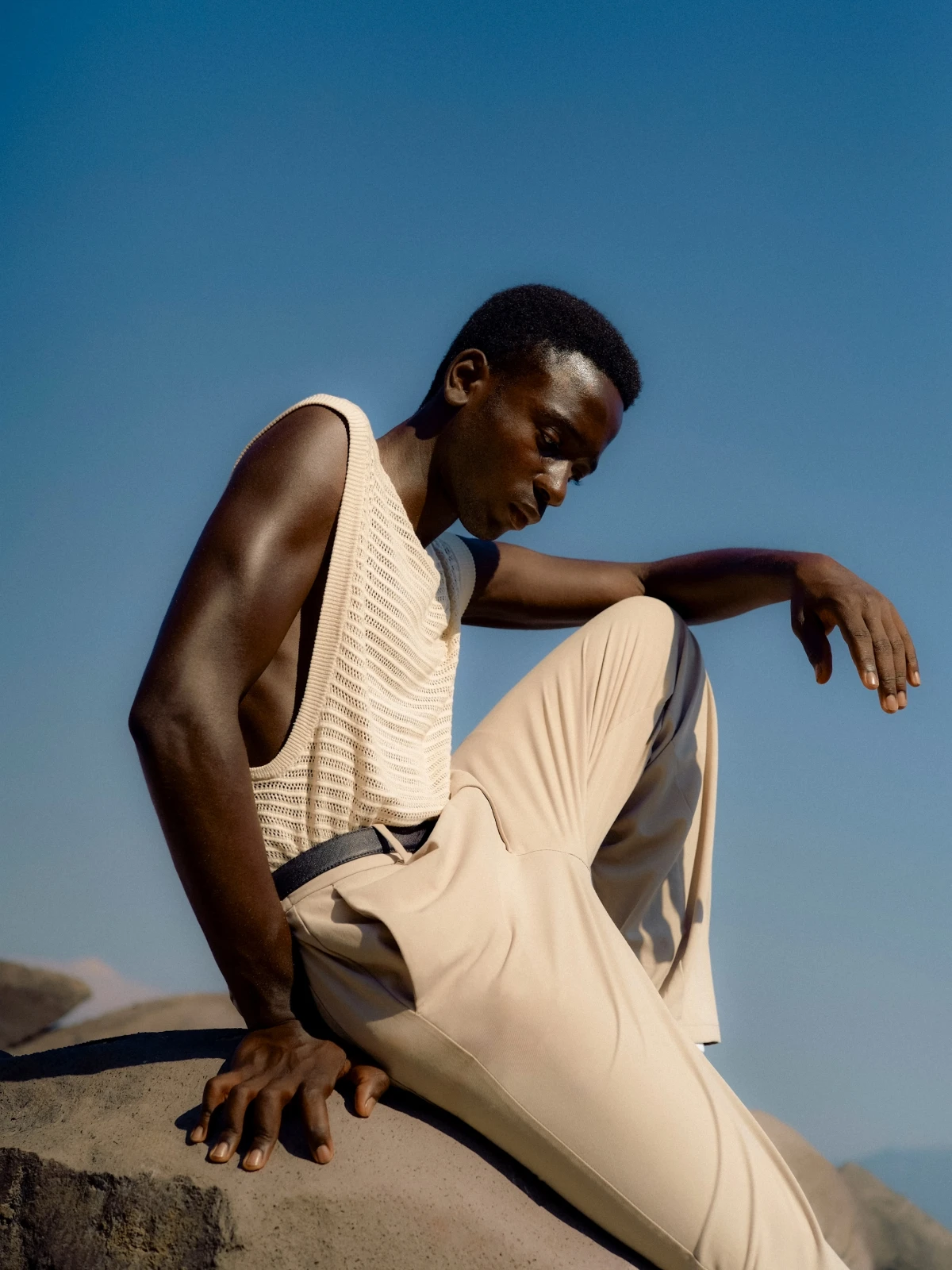 Male model in cream Prada look posed on rocks under blue sky for luxury fashion campaign