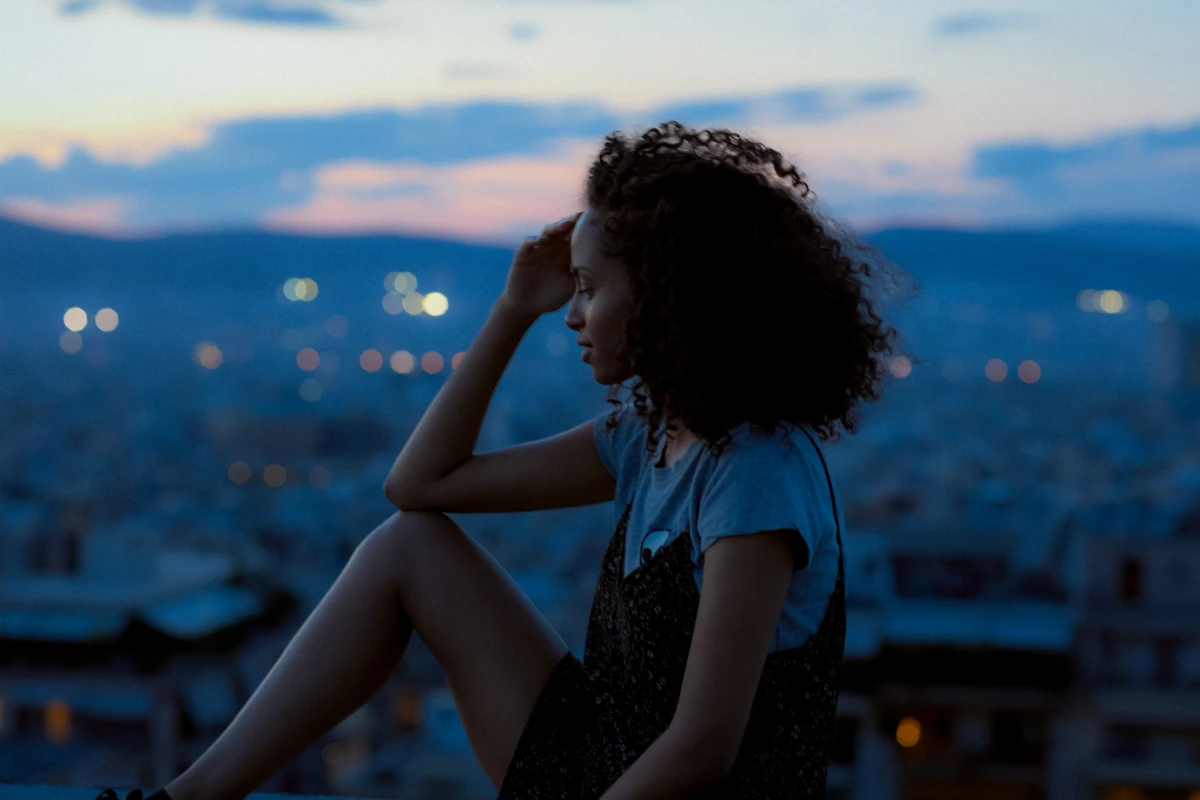 Young woman sitting on rooftop at dusk overlooking Athens city lights for Becks urban lifestyle campaign